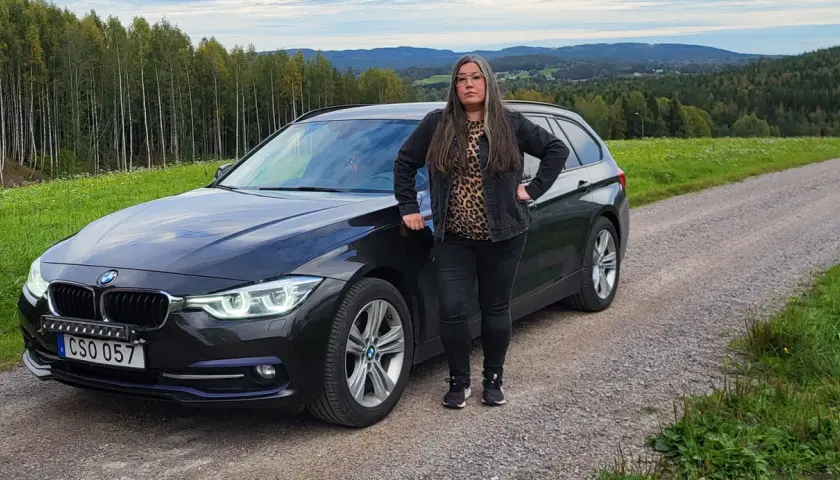 Kvinna vid en svart BMW kombi i svensk landsbygd. Kanske ett bmw b47 problem som gör att hon stannat här.