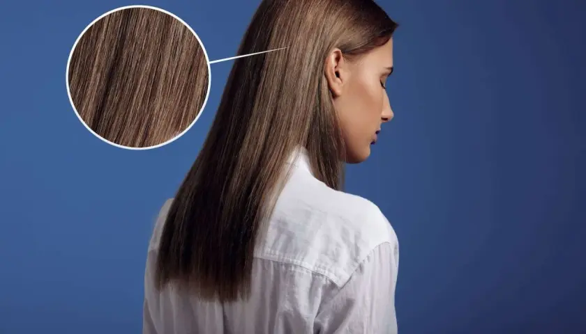 Primer plano de un cabello castaño sedoso, con un círculo que amplía los detalles. Parece que el pelo está en pausa, esperando un nuevo estilo.