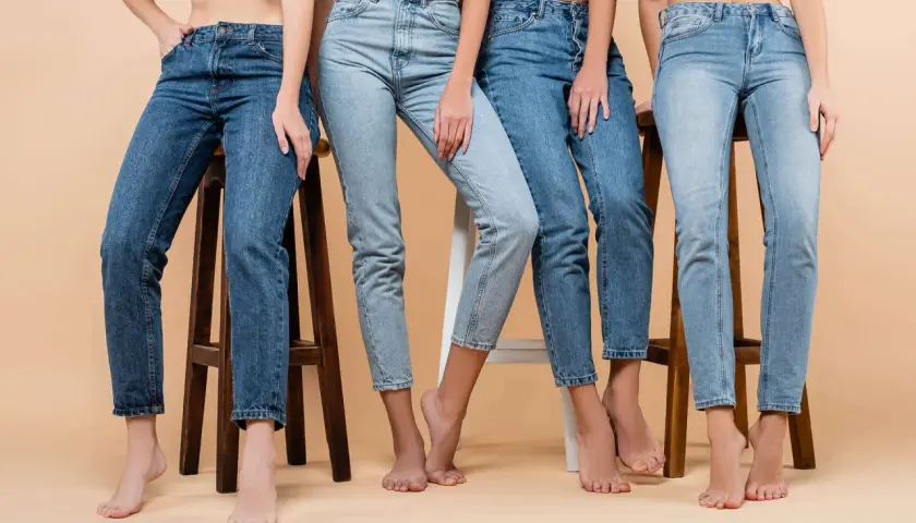 Cztery kobiety w różnych odcieniach jeansów siedzą na stołkach. Denim to materiał, który nigdy nie wychodzi z mody.