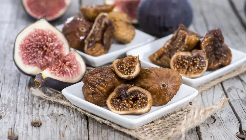 Des figues fraîches et des figues séchées au four sur des assiettes blanches, posées sur du bois rustique.