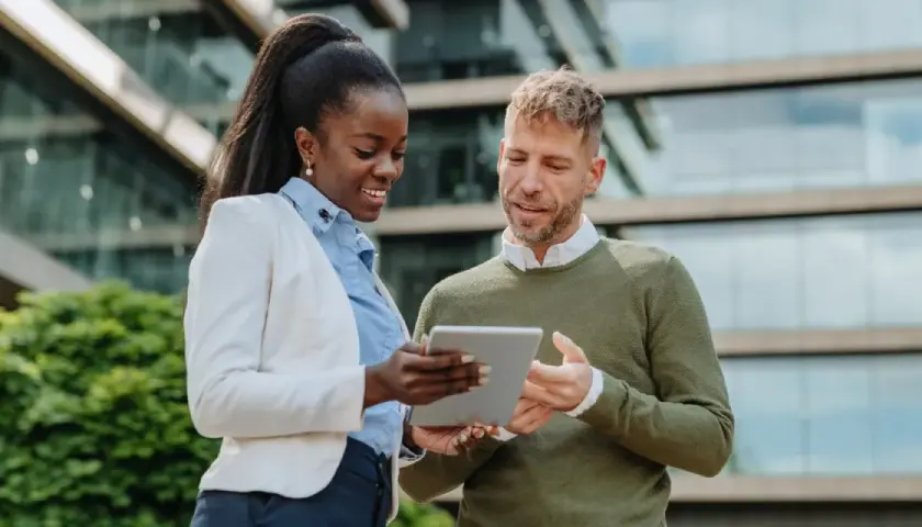 Two professionals discuss their MPA online program on a tablet outside a modern building.