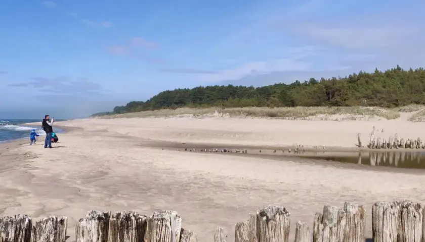 Piękna plaża w Dąbkach, idealne miejsce na rodzinne atrakcje. Ojciec z dzieckiem spacerują brzegiem morza.