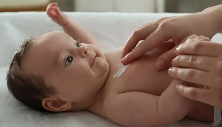 Delikatna pielęgnacja 12 tygodniowego dziecka. Krem na jego skórze, czułe dłonie mamy.