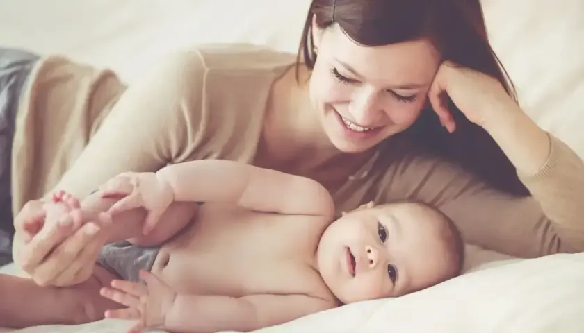 Uśmiechnięta mama na urlopie macierzyńskim bawi się nóżkami swojego dziecka.