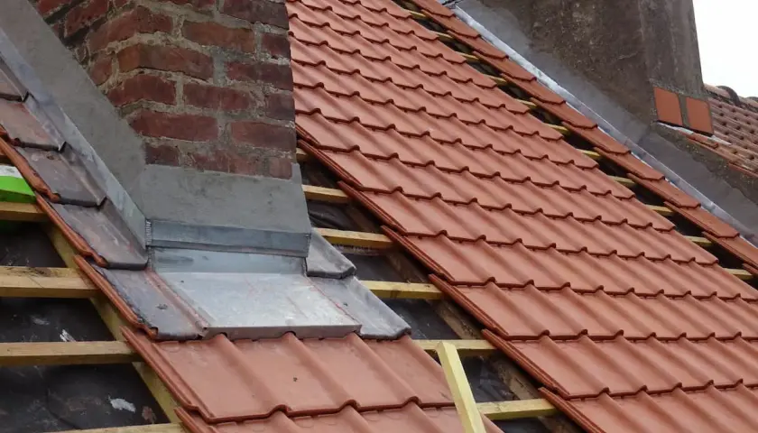 Dachdecker arbeiten am Kamin, um ihn einbleien. Neue rote Dachziegel werden verlegt.