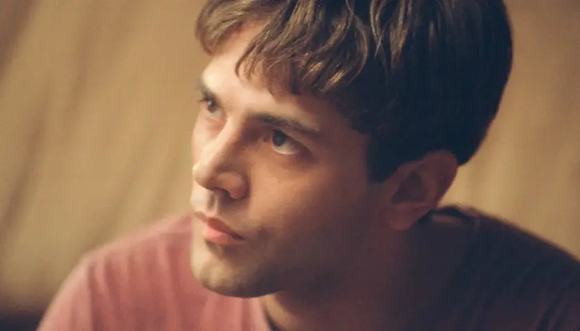 Primo piano di un giovane uomo con capelli castani e una maglietta rosa. Potrebbe essere Xavier Dolan fidanzato.