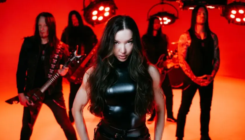 Arch enemy wokalistka w skórzanym stroju, otoczona przez zespół na tle czerwonych świateł.