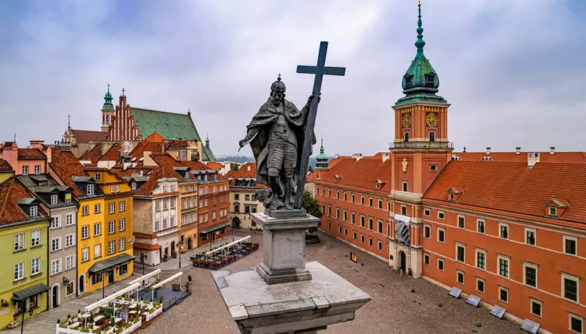 Pomnik króla Zygmunta III Wazy na placu Zamkowym, w tle Zamek Królewski i kolorowe kamienice Starego Miasta. Dwie wieże Warszawy w oddali.