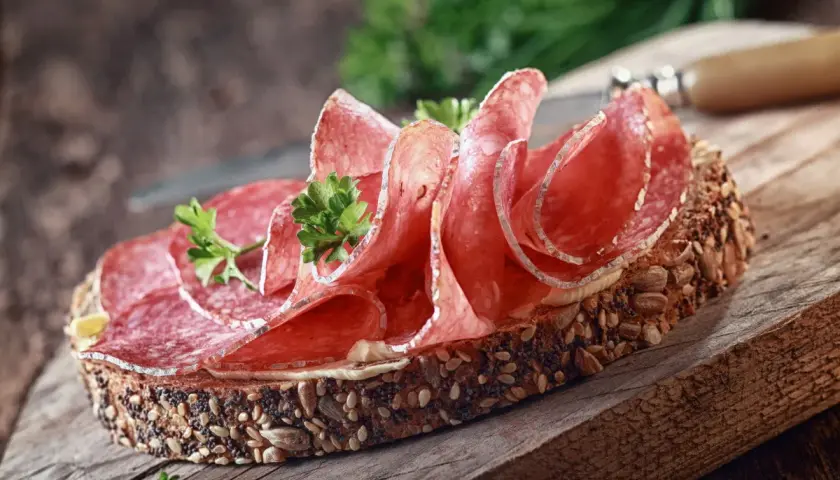 Kanapka z ciemnego pieczywa obficie posypanego ziarnami, z plasterkami aromatycznego salami i natką pietruszki.