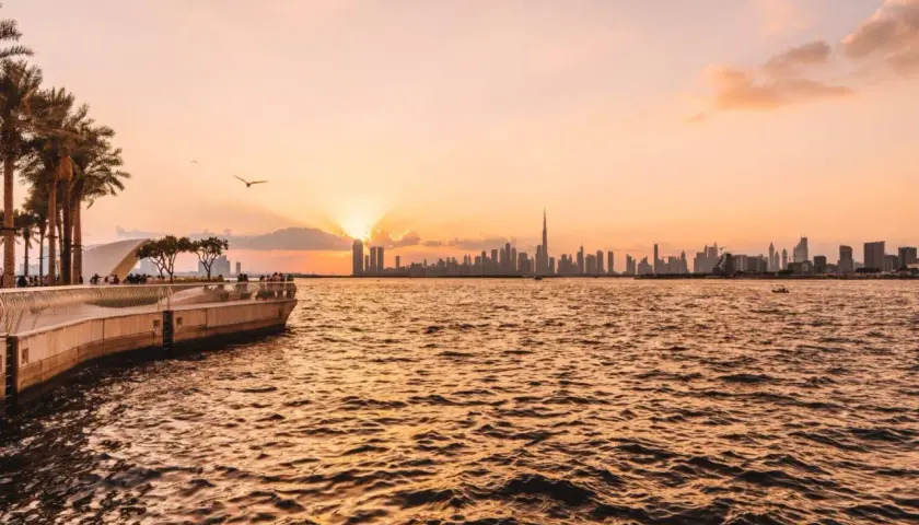 Sonnenuntergang über Dubai. Die Skyline mit dem Burj Khalifa und Palmen am Ufer sind einige der Dubai Highlights.