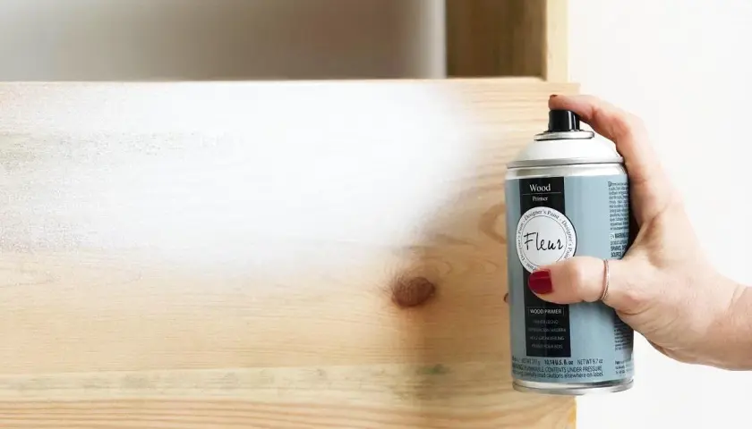Mano aplica imprimación en spray a madera. Es necesario imprimar antes de pintar madera para un acabado perfecto.
