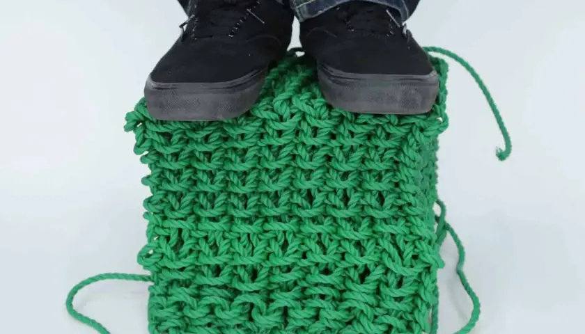Pieds chaussés sur un cube de tricotage 3D vert vif, démontrant la solidité de la maille.
