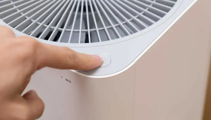 Dedo presionando el botón de encendido de un purificador de aire con filtro de ozono.