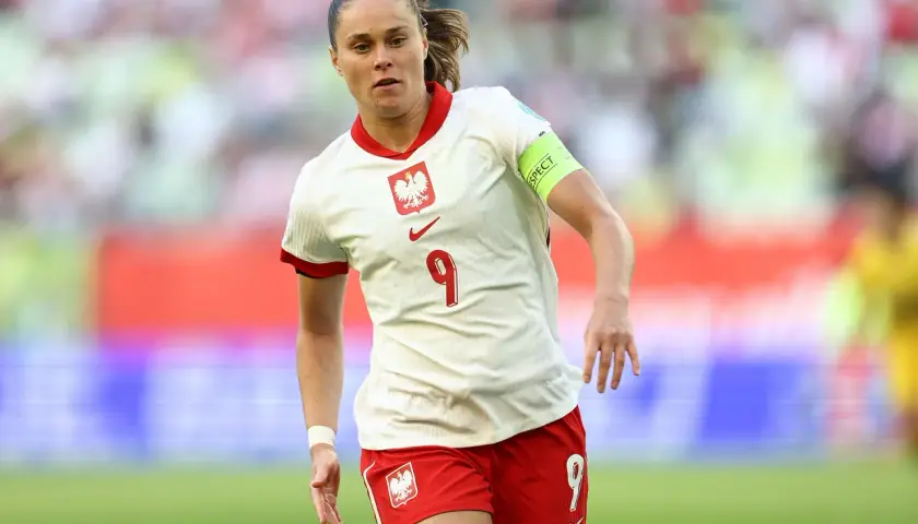 Piłkarka w białej koszulce z orłem i numerem 9, w czerwonych spodenkach. Reprezentuje polska dania na boisku.
