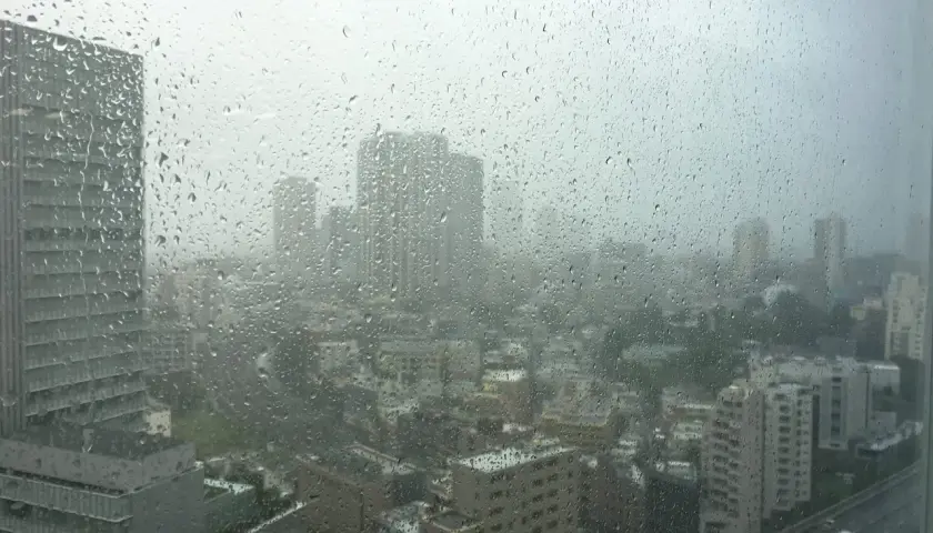 Regen prasselt auf ein Fenster mit Blick auf eine Stadt in Japan. Die Sicht ist durch die Tropfen und den grauen Himmel getrübt, typisch für die japan taifun saison.