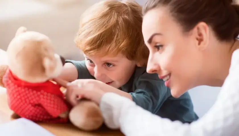 Uśmiechnięta opiekunka dziecięca praca z chłopcem i pluszowym misiem.