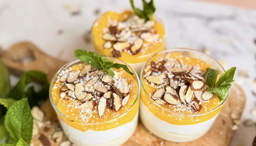 Drei Gläser mit cremigem Kokos Dessert vegan, garniert mit Mango-Püree, Mandelblättchen und Kokosraspeln.
