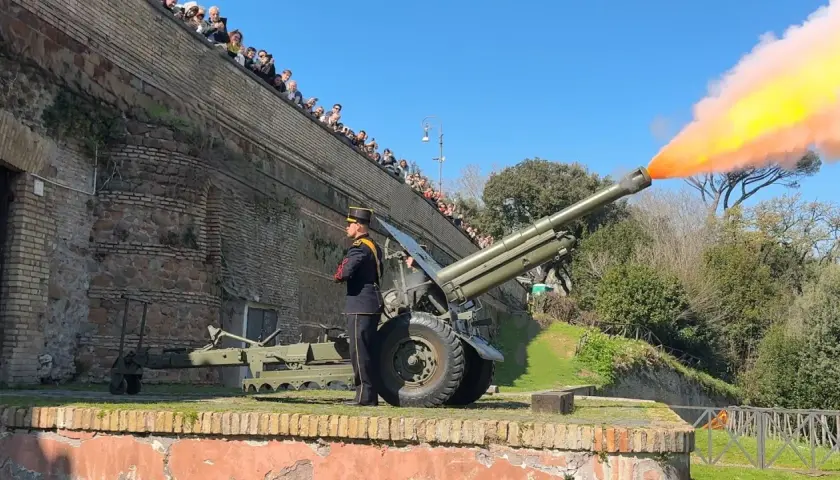 Il cannone Gianicolo spara una palla di fumo arancione e gialla. Un soldato in uniforme osserva, mentre una folla guarda dall'alto.