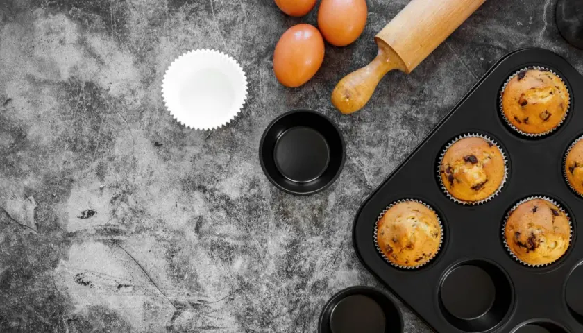 Gotowe muffinki w foremkach do ciast, jajka i wałek do ciasta na kamiennym blacie.