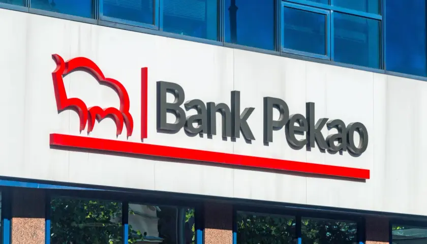 Logo Banku Pekao na białej fasadzie budynku, z niebieskimi oknami powyżej.