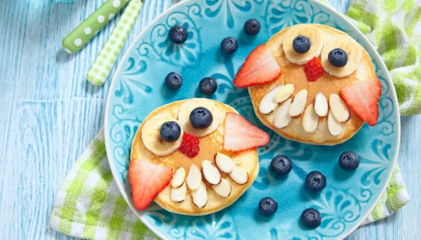 Due pancake a forma di gufo, decorati con frutta e mandorle, per una colazione sana bambini.