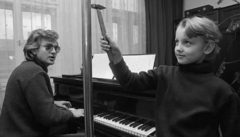 Zbigniew Wodecki gra na pianinie, a Paweł Wodecki trzyma młotek, jakby chciał uderzyć w klawisze.