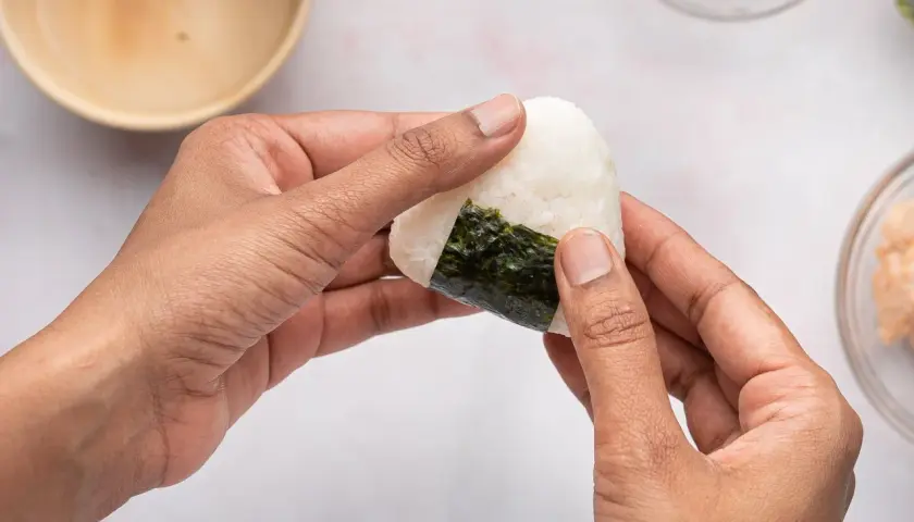 Hands shaping a perfectly sized onigiri, a delicious rice ball wrapped in nori seaweed.