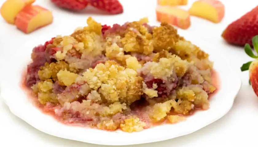 Ein Teller mit warmem Erdbeer-Crumble, garniert mit frischen Erdbeeren und Apfelstücken.