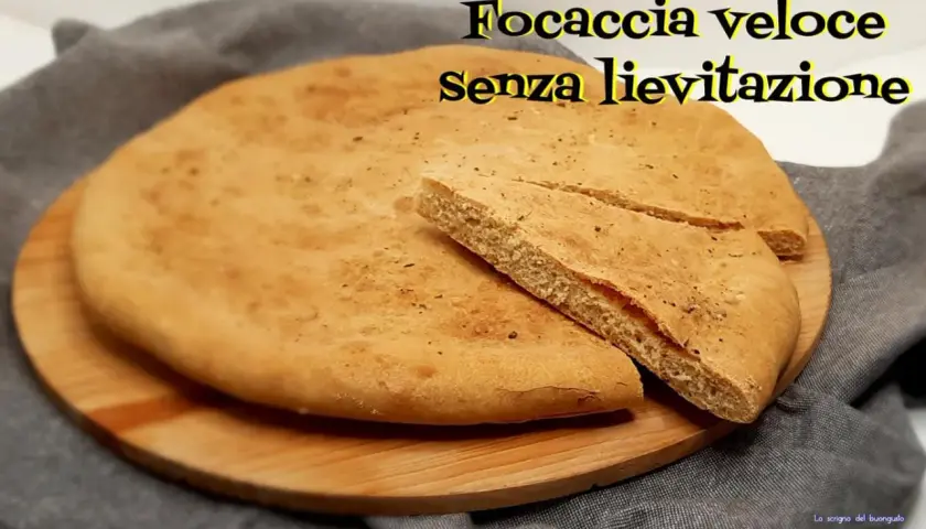 Focaccia veloce senza lievitazione su tagliere di legno. Una fetta è stata tagliata per mostrare la morbidezza.