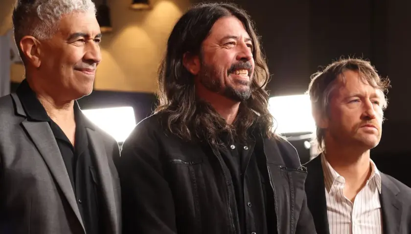 Trzech członków Foo Fighters: Nate Mendel, Dave Grohl i Chris Shiflett, uśmiechają się i patrzą w bok.