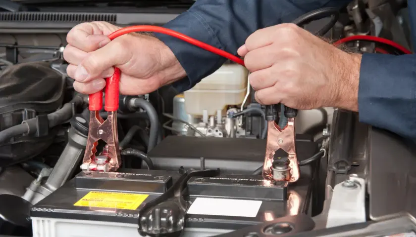 Podłączanie kabli rozruchowych do akumulatora 24v. Mechanik w ciemnej koszuli podłącza czerwone kable do biegunów akumulatora samochodowego.