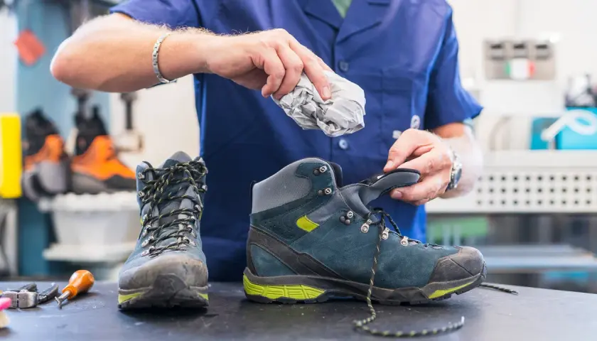 A person stuffs crumpled paper into a hiking boot, demonstrating the best way to dry boots after a muddy adventure.