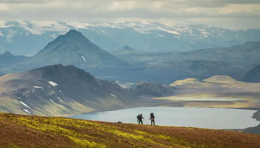 Two hikers on a self-guided Laugavegur trail adventure, with a serene lake and dramatic mountains in the background.