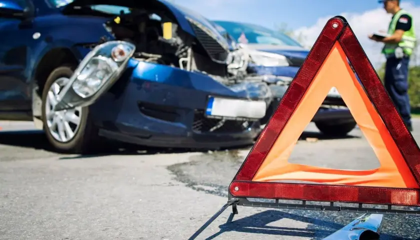 Triangolo di emergenza davanti a due auto danneggiate dopo un incidente. Un poliziotto documenta i danni, forse un incidente senza assicurazione.