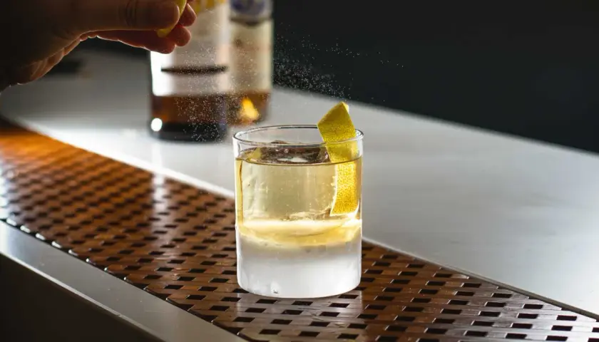 Un barista completa la negroni ricetta bar con una scorza di limone. Ghiaccio e liquore dorato in un bicchiere.