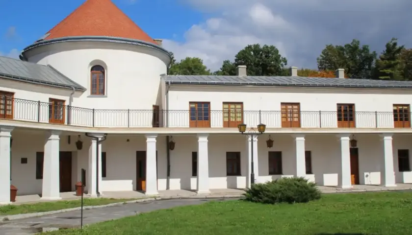 Zamek w Lesku, biały budynek z okrągłą wieżą i pomarańczowym dachem, otoczony zielenią.