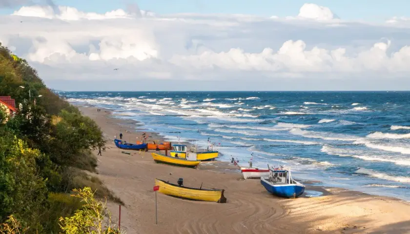 Kolorowe łodzie rybackie na piaszczystej plaży, falujące polskie morze i zielone wzgórze.