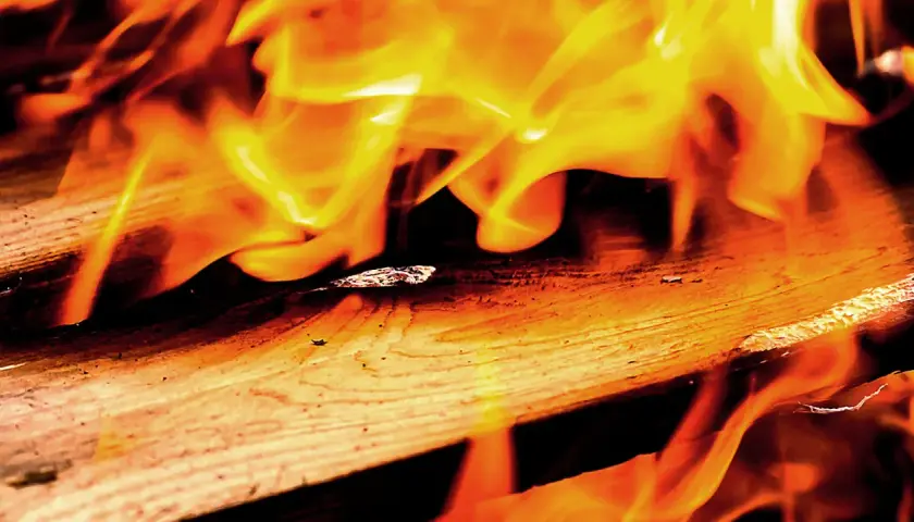 Flammen tanzen über Holz. Lackiertes Holz verbrennen giftig, hinterlässt Asche und Rauch.