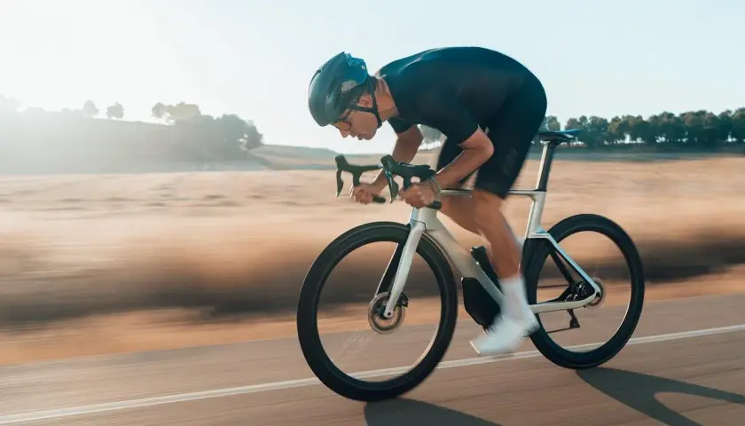 Kolarz w aerodynamicznej pozycji minimalizuje opory toczenia opon rowerowych, pędząc przez krajobraz.
