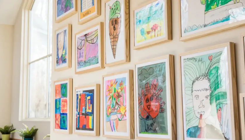 A vibrant kids art gallery wall showcases colorful drawings of ice cream, flowers, and portraits, all framed in light wood.