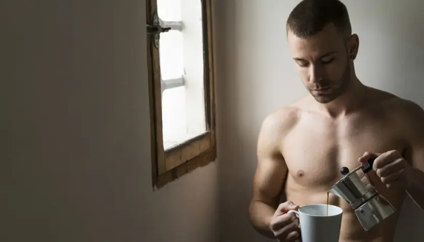 Uomo nudo versa caffè, riflessione sulla psicologia di un uomo sposato. Luce soffusa da una finestra.