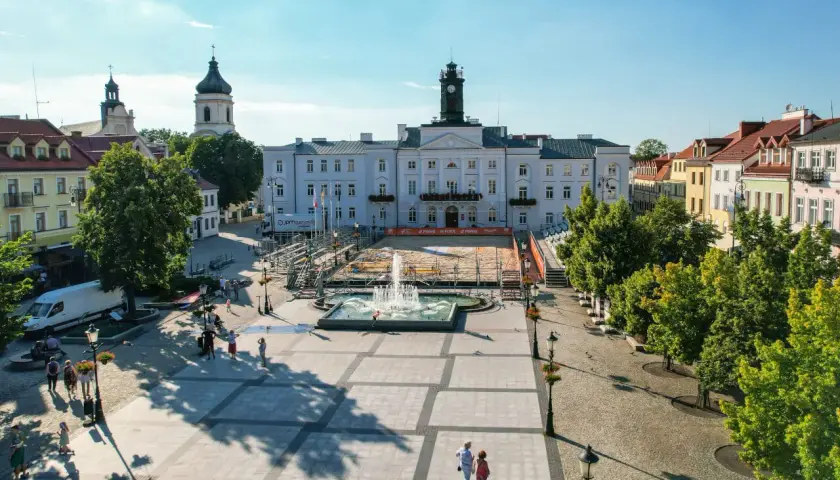 Stary Rynek Płock z ratuszem i fontanną w centrum. W tle widać kościoły i kolorowe kamienice.