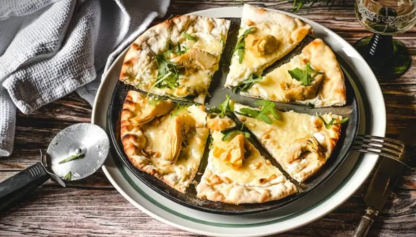 Eine köstliche Pizza Bianca mit Artischocken, Rucola und Pinienkernen, bereit zum Genießen.