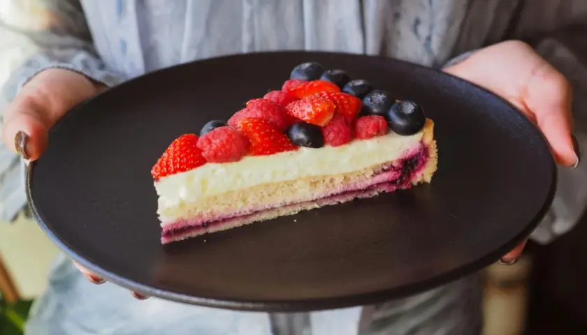 Tranche de tarte aux fruits rouges sur une crème mousseline onctueuse, présentée sur une assiette noire.