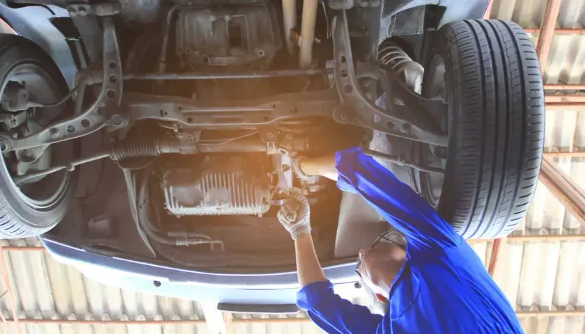 Mechanik pracuje pod samochodem, regulując układ kierowniczy. Dowiedz się, jak skasować luz na maglownicy.