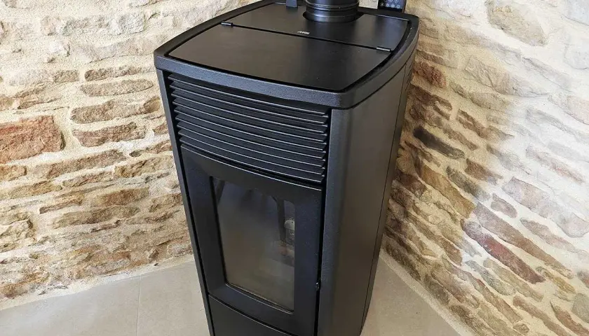 Poêle à granulés noir moderne, avec écran de contrôle, adossé à un mur de pierres. Apprenez comment éteindre un poêle à granulé en toute sécurité.