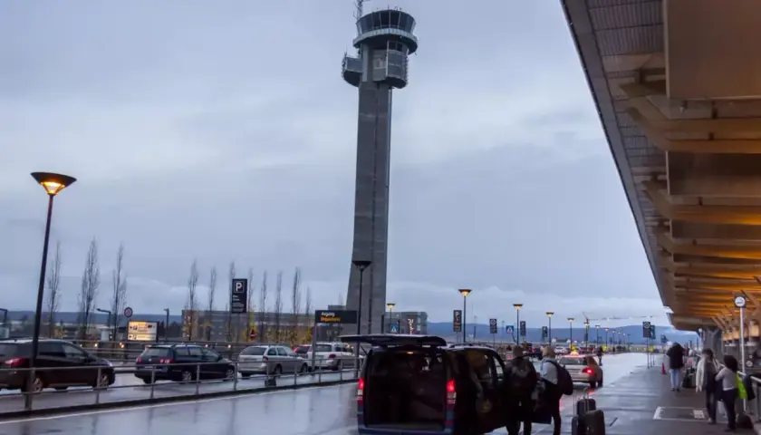 Wieża kontrolna na oslo lotnisko góruje nad mokrym asfaltem i samochodami. Ludzie z bagażami wsiadają do vana.