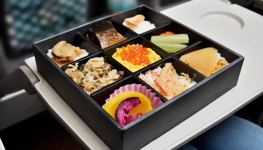 A delicious train bento box filled with various Japanese delicacies, including grilled fish, seafood, and colorful roe, ready for a journey.