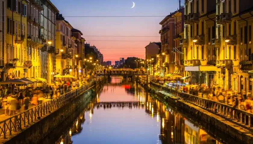 Atardecer en los Navigli de Milán, con gente paseando y luces reflejándose en el canal.