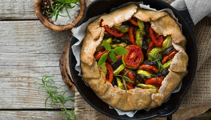 Une rustique quiche aux légumes, garnie de tomates, courgettes et aubergines, prête à être dégustée.